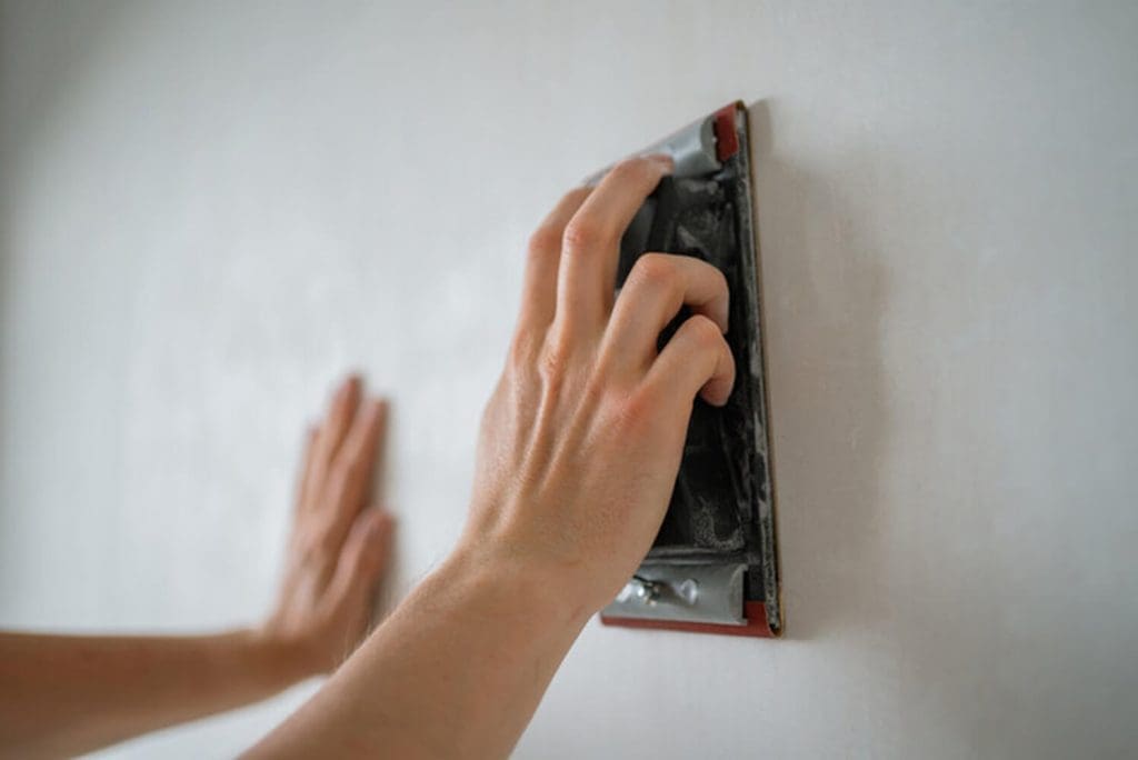 A person sanding an interior wall as part of the surface preparation process before interior painting.