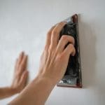 A person sanding an interior wall as part of the surface preparation process before interior painting.