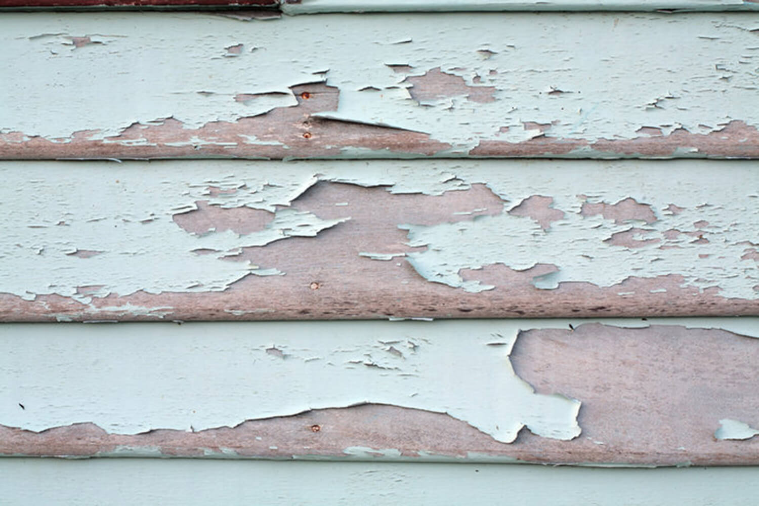 Severely peeling and flaking exterior paint on wood siding showing signs of coating failure.
