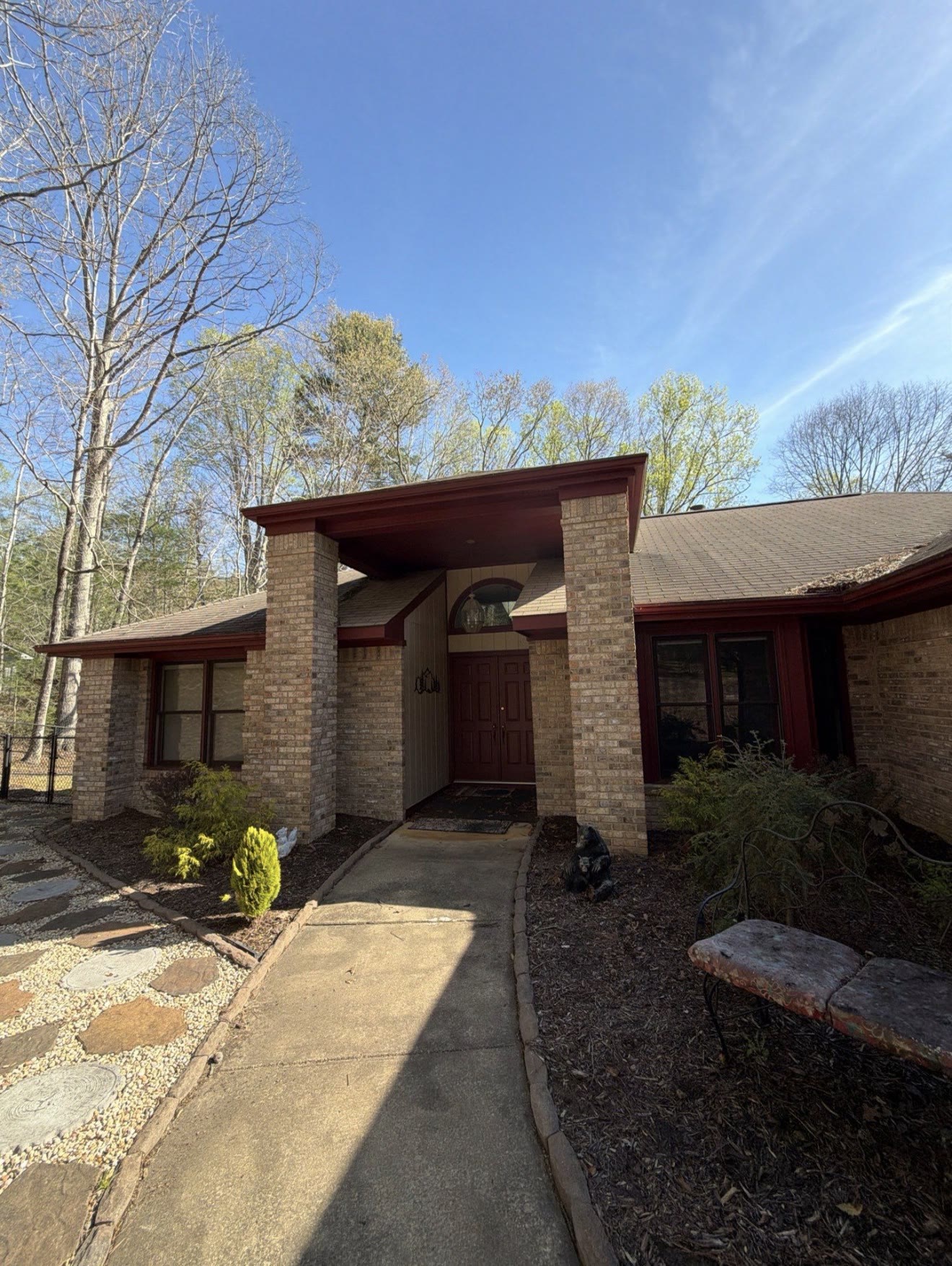Single-story home exterior with natural stone pillars, a curved stone walkway, and lush trees under a blue sky, painted by A2 Painting in Hendersonville NC