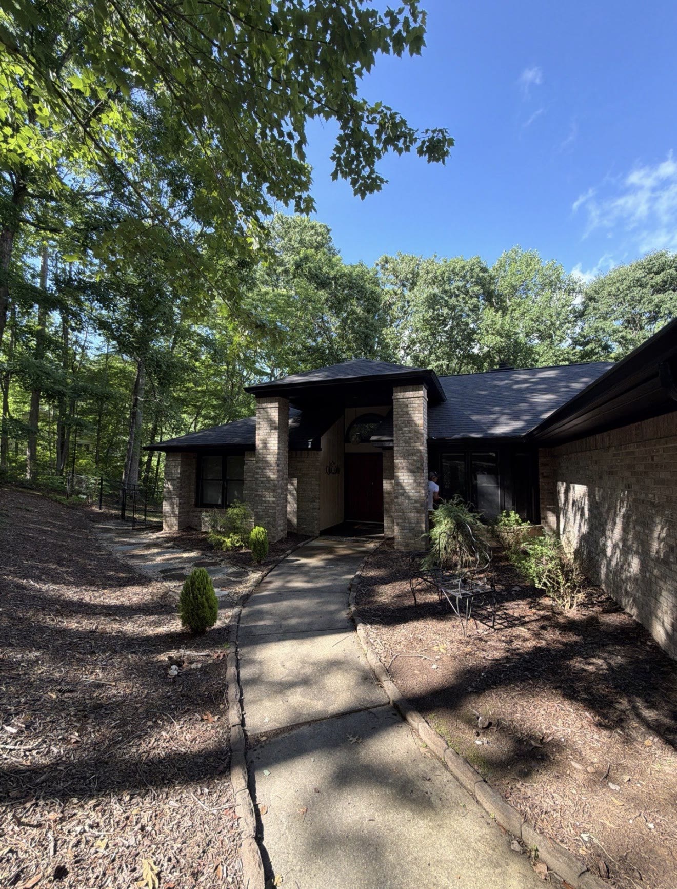 Single-story home exterior with dark siding, a curved stone pathway, and lush green trees under a partly cloudy sky, painted by A2 Painting in Hendersonville NC