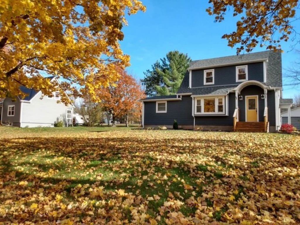 A two-story home with dark blue siding surrounded by fall foliage, illustrating the seasonal window for exterior house painting.