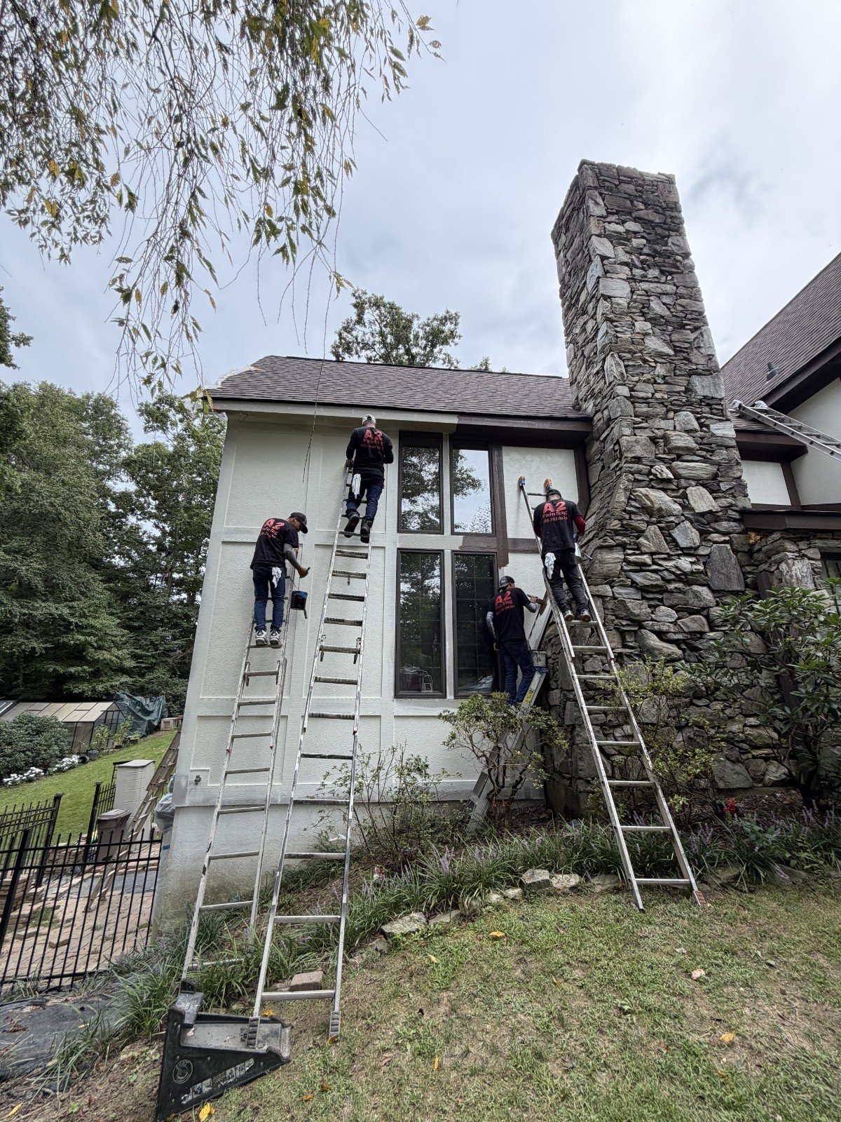 A2 Painting crew working together on extension ladders to paint the exterior walls of a multi-story home in Hendersonville, NC