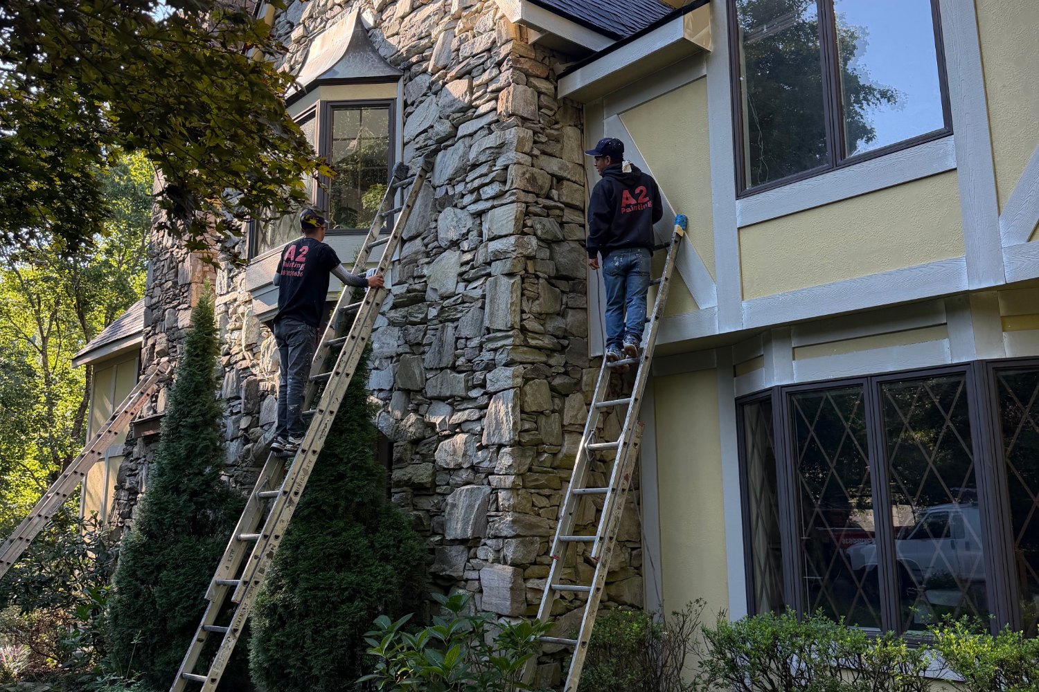 A2 Painting crew on ladders painting a large stone home exterior