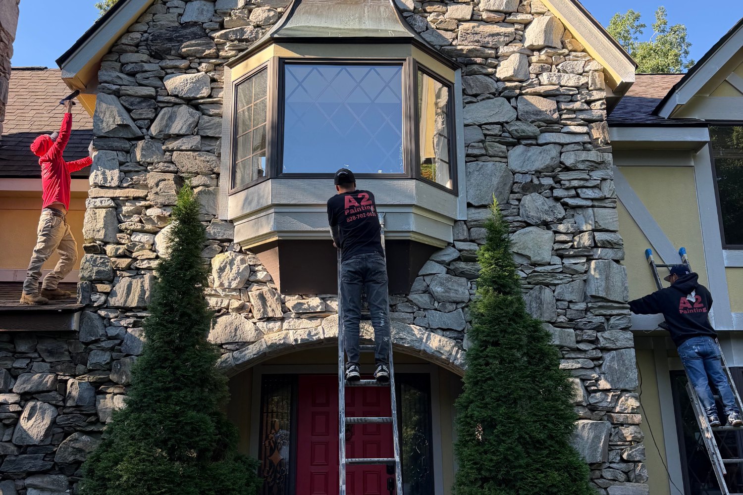 A2 Painting crew in branded shirts painting a stone home front