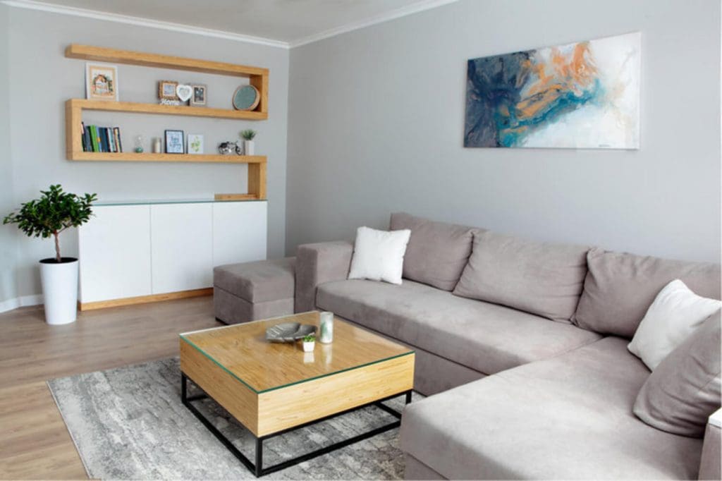 A staged neutral-toned living room with gray walls, a sectional sofa, and natural wood accents, illustrating how interior paint color affects home value.