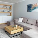 A staged neutral-toned living room with gray walls, a sectional sofa, and natural wood accents, illustrating how interior paint color affects home value.